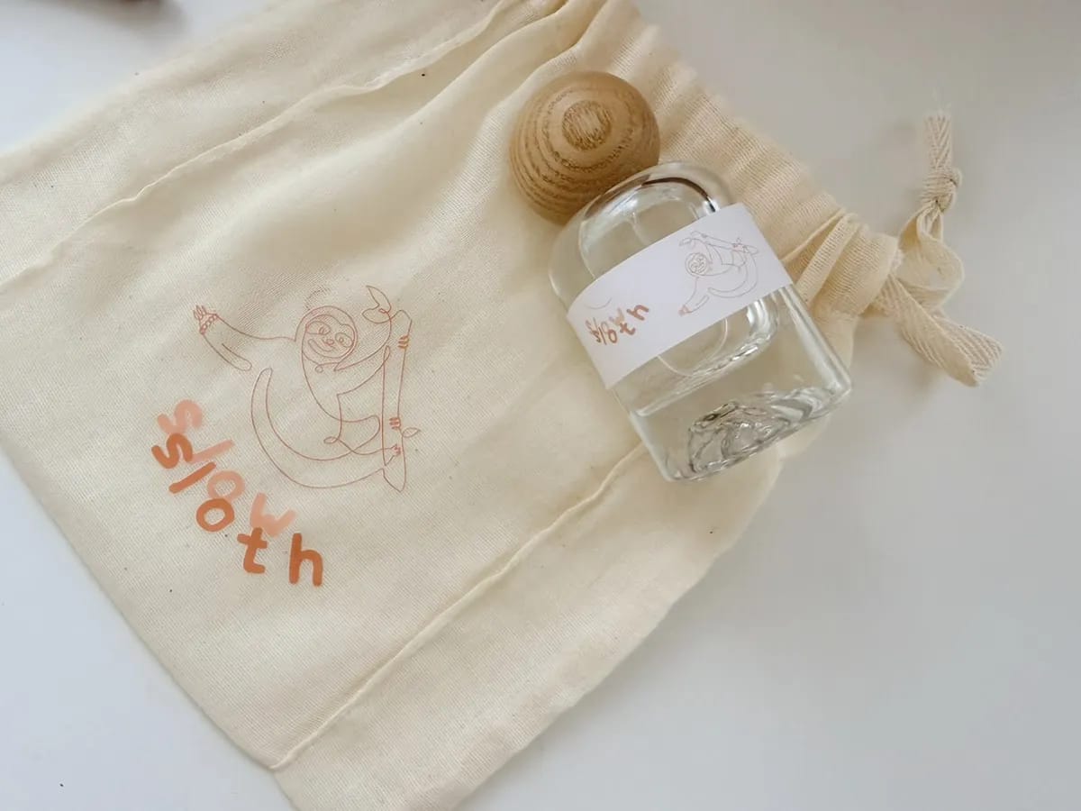 Slow Sloth perfume bottle beside a branded cotton pouch