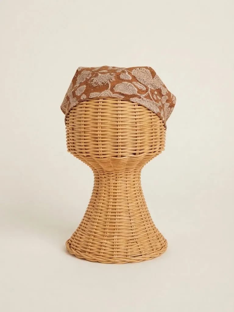 Earth-brown cotton bandana with cream botanical block print on a woven display head